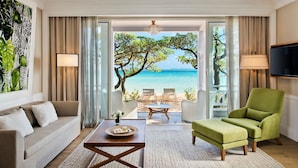 Una habitación con sofá, sillón verde, una mesa de centro y vistas a la playa.