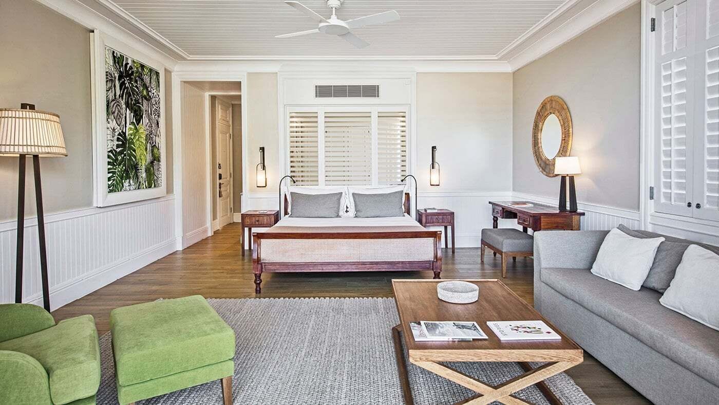 A bedroom with a bed, bedside tables, a green chair, a grey sofa, and a ceiling fan.