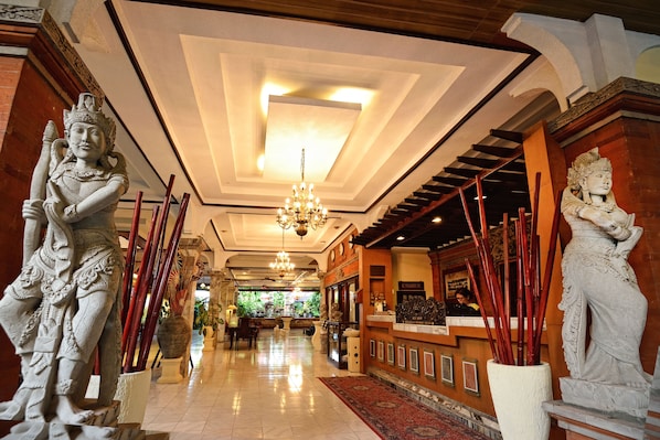 A grand lobby with a chandelier, statues, a reception desk, and a cash register.