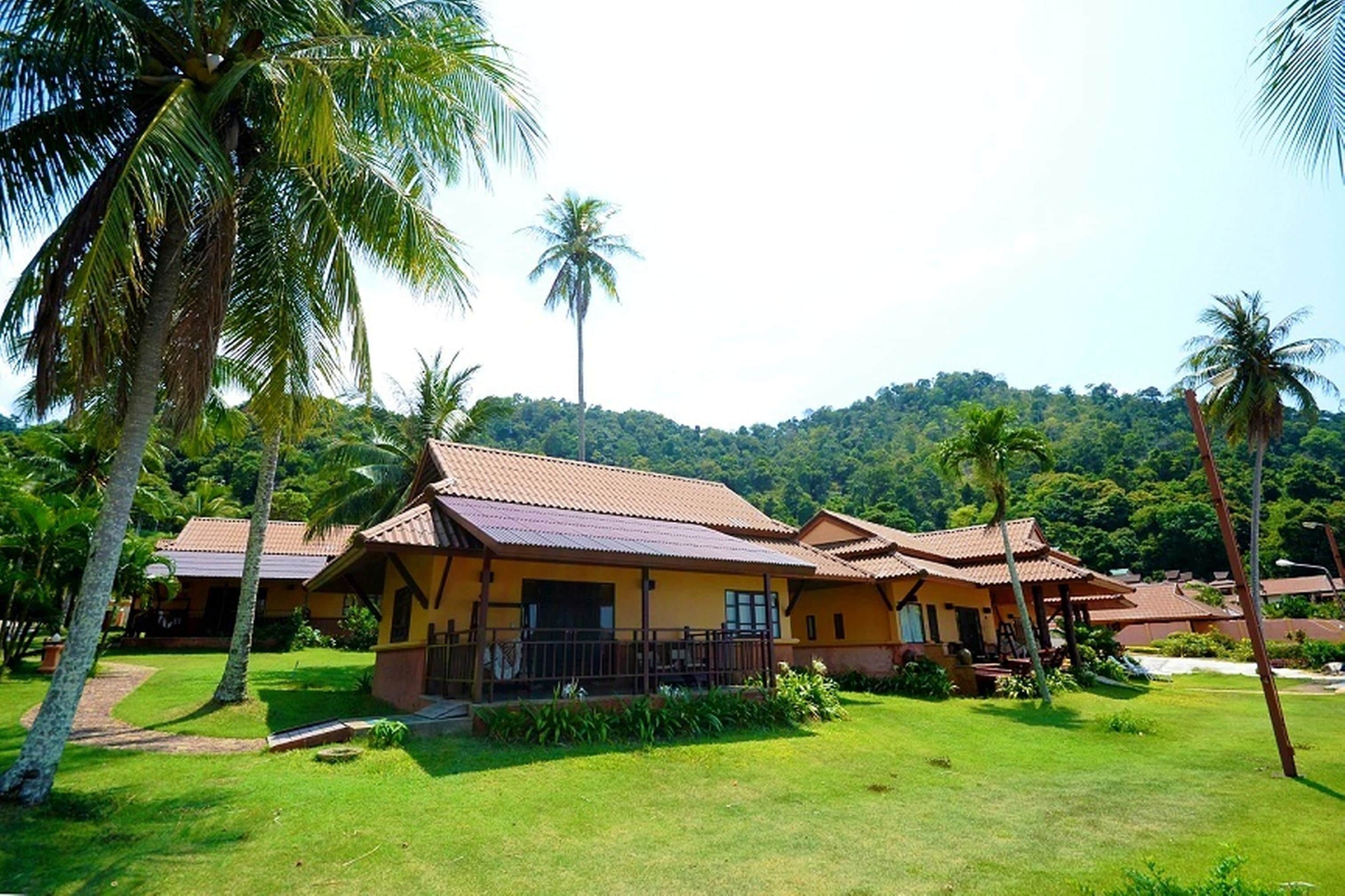 A resort with multiple buildings, each featuring a tiled roof and surrounded by lush greenery and palm trees.