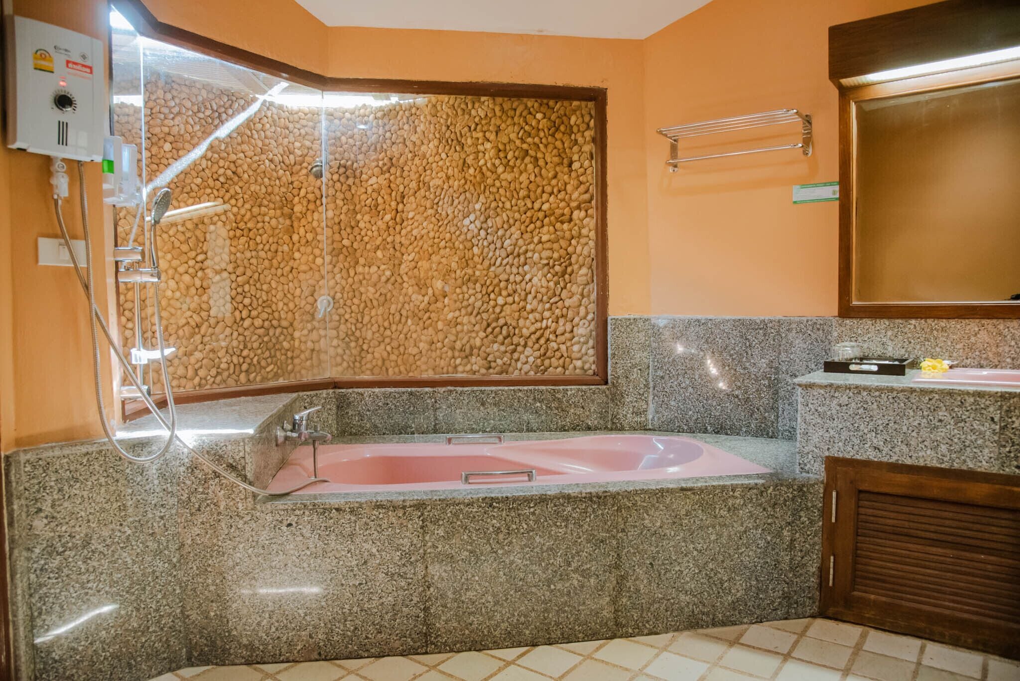 A bathroom with a granite countertop, a pink bathtub, a wooden door, and a wall-mounted mirror.