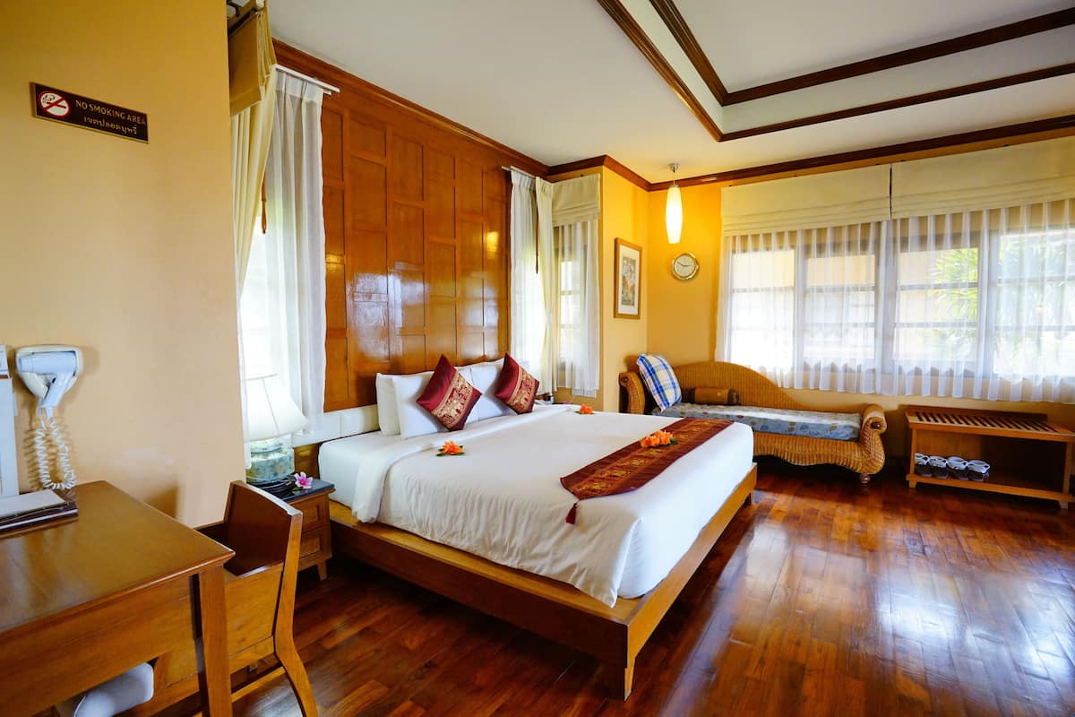 Hotelkamer met een houten bed, een bureau met telefoon, een stoel, een bank en een schoenenrek.