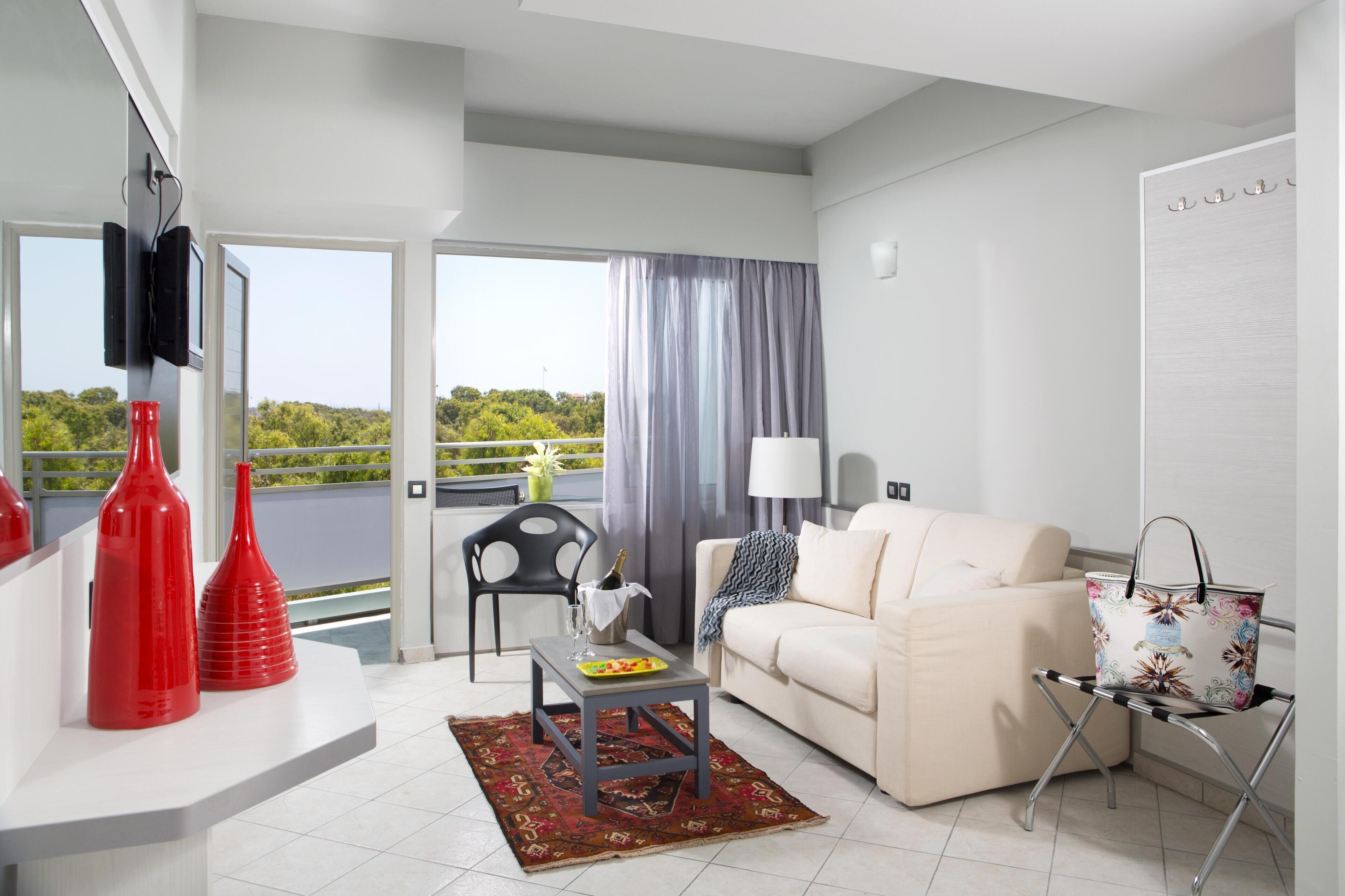 Un salon moderne avec un canapé, une table basse et un téléviseur fixé au mur. Il y a un balcon avec vue sur la verdure.