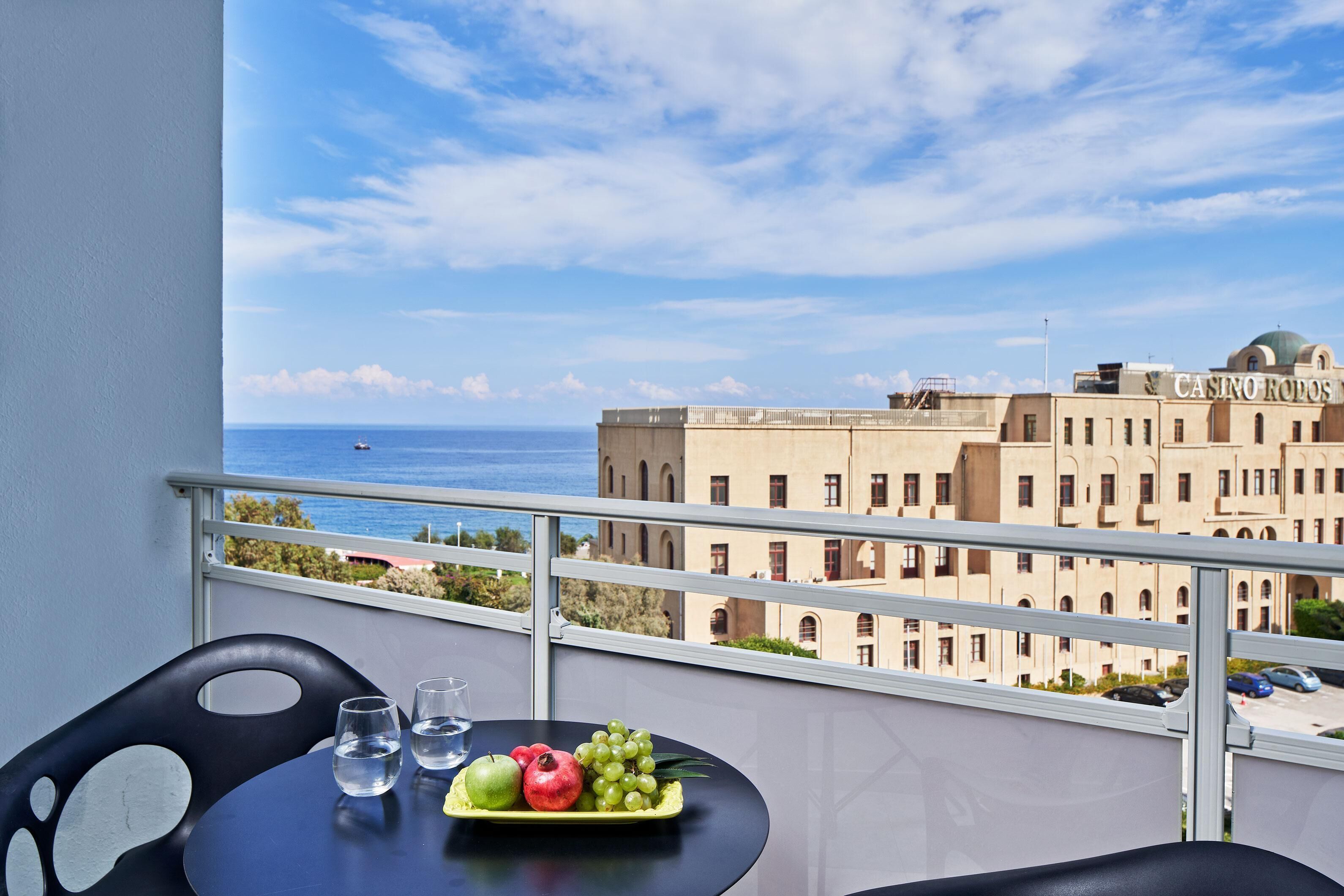 Ein Balkon mit Tisch, gedeckt mit Wassergläsern und einer Obstplatte, mit Blick auf ein Gebäude mit Casino-Schild.