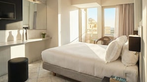 Ein Hotelzimmer mit Bett, Schreibtisch, Stuhl und einem Fenster mit Blick auf Gebäude.