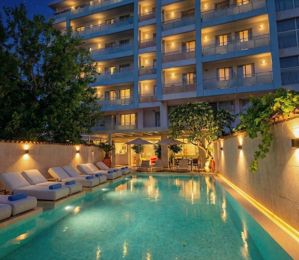 A hotel with a swimming pool, lounge chairs, and a bar area.