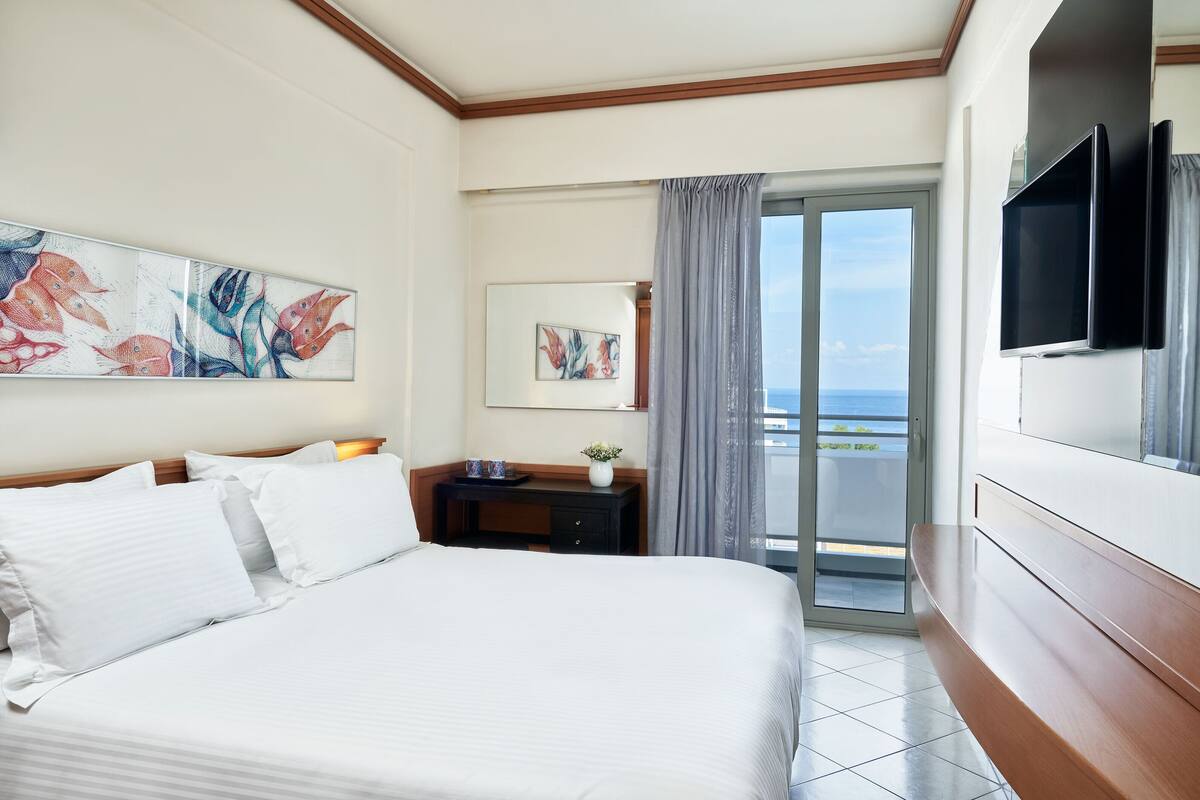 Ein Hotelzimmer mit einem großen Bett, einem Schreibtisch, einem Fernseher und einem Balkon mit Blick.