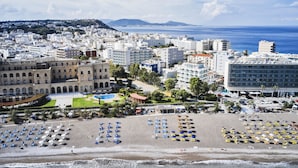 Eine Küstenstadtlandschaft mit Strandabschnitt, zahlreichen Sonnenschirmen und Booten.
