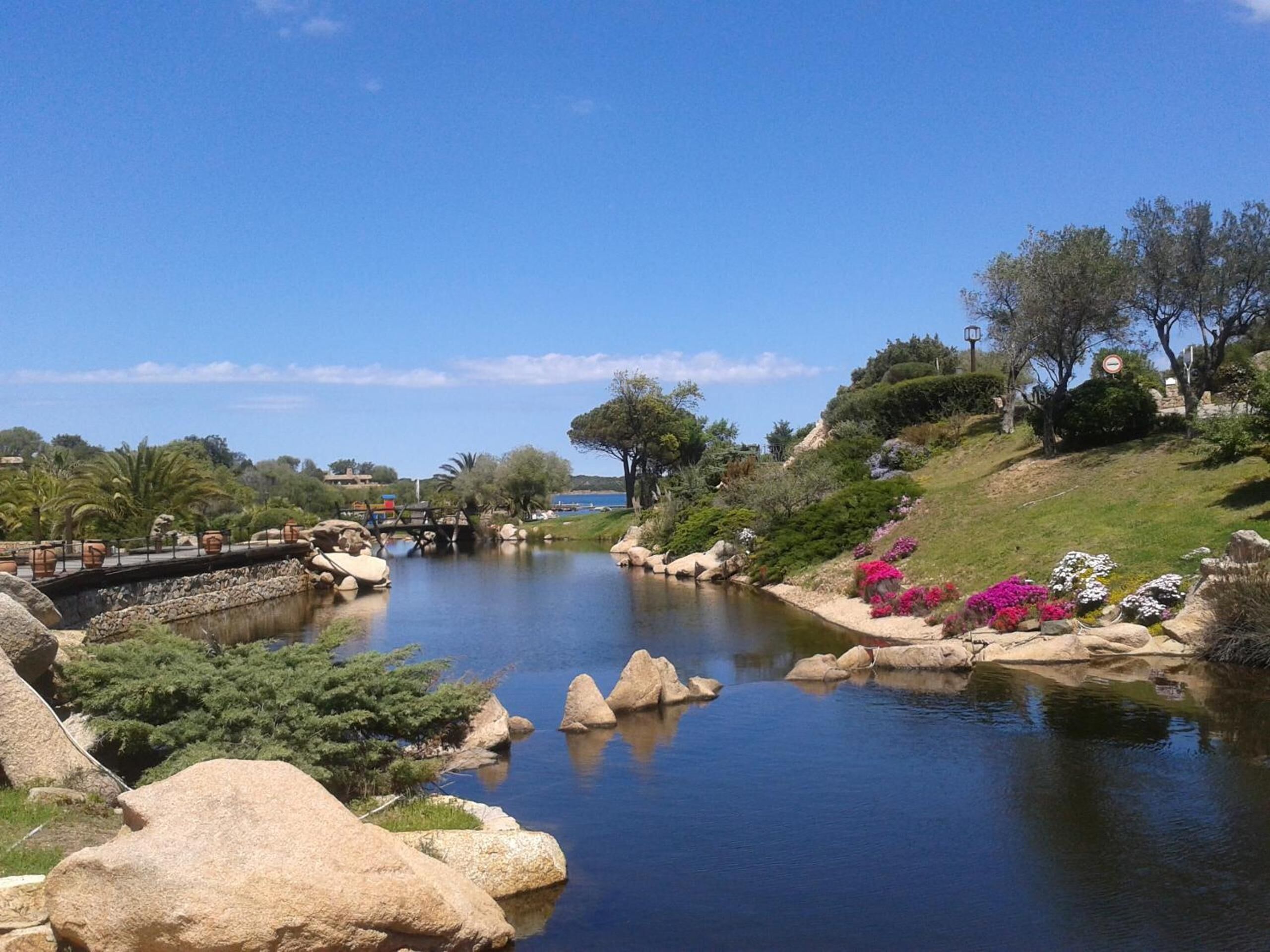 Un paisaje tranquilo junto al río, con un puente, abundante vegetación y cielo despejado.