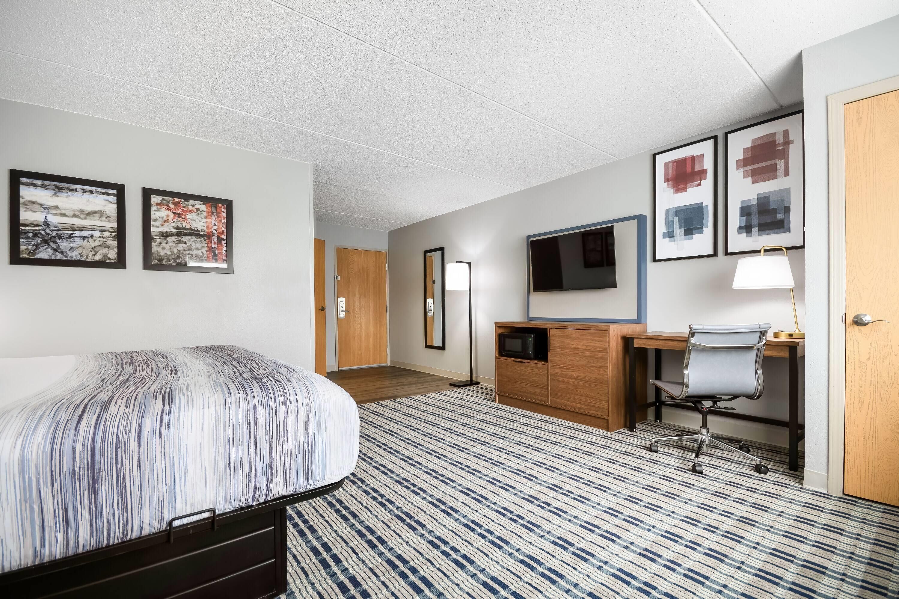 Habitación de hotel con cama, escritorio, silla, televisión y obras de arte en las paredes.