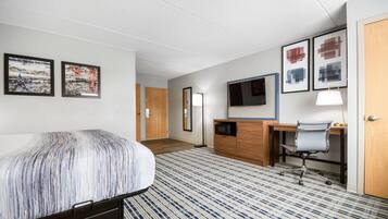 A hotel room with a bed, a desk, a chair, a TV, and artwork on the walls.