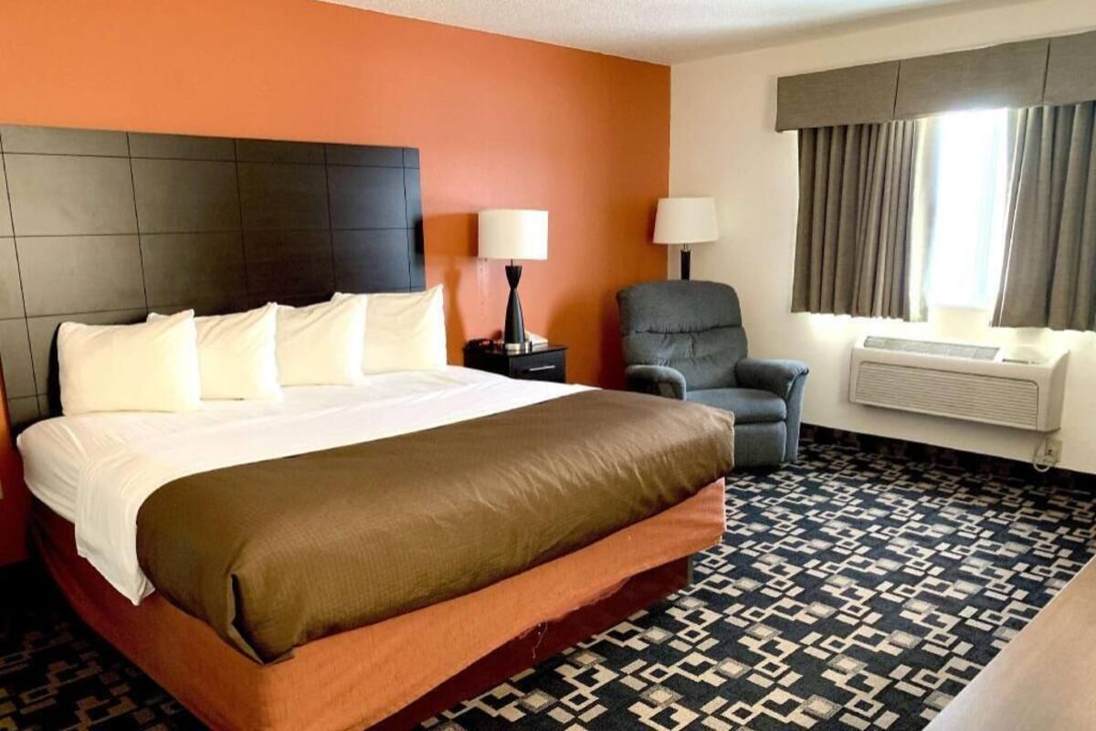 Hotelkamer met een bed, twee nachtkastjes, een stoel, een airconditioning en een raam met gordijnen.