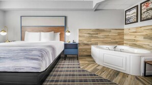 Ein modernes Hotelzimmer mit einem großen Bett, einem Nachttisch mit Lampen, einer integrierten Badewanne und einer Holzpaneele verkleideten Wand.