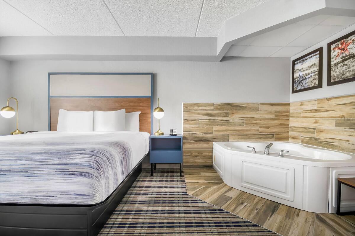 Een moderne hotelkamer met een groot bed, een nachtkastje met lampen, een ingebouwd bad en een houten wandpaneel.