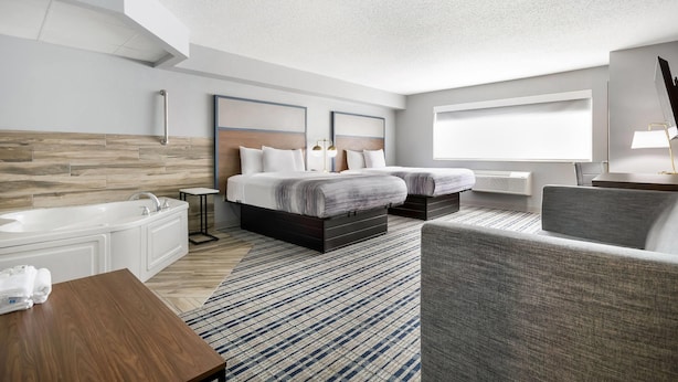 Ein modernes Hotelzimmer mit einem großen Bett, einem Einzelbett, einer Sitzecke, einem Badezimmer mit Badewanne und einem großen Fenster für natürliches Licht.
