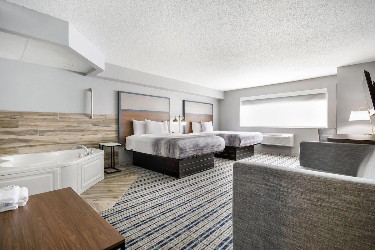 Een moderne hotelkamer met een groot bed, een bijzetbed, een zithoek, een badkamer met bad en een groot raam dat natuurlijk licht biedt.