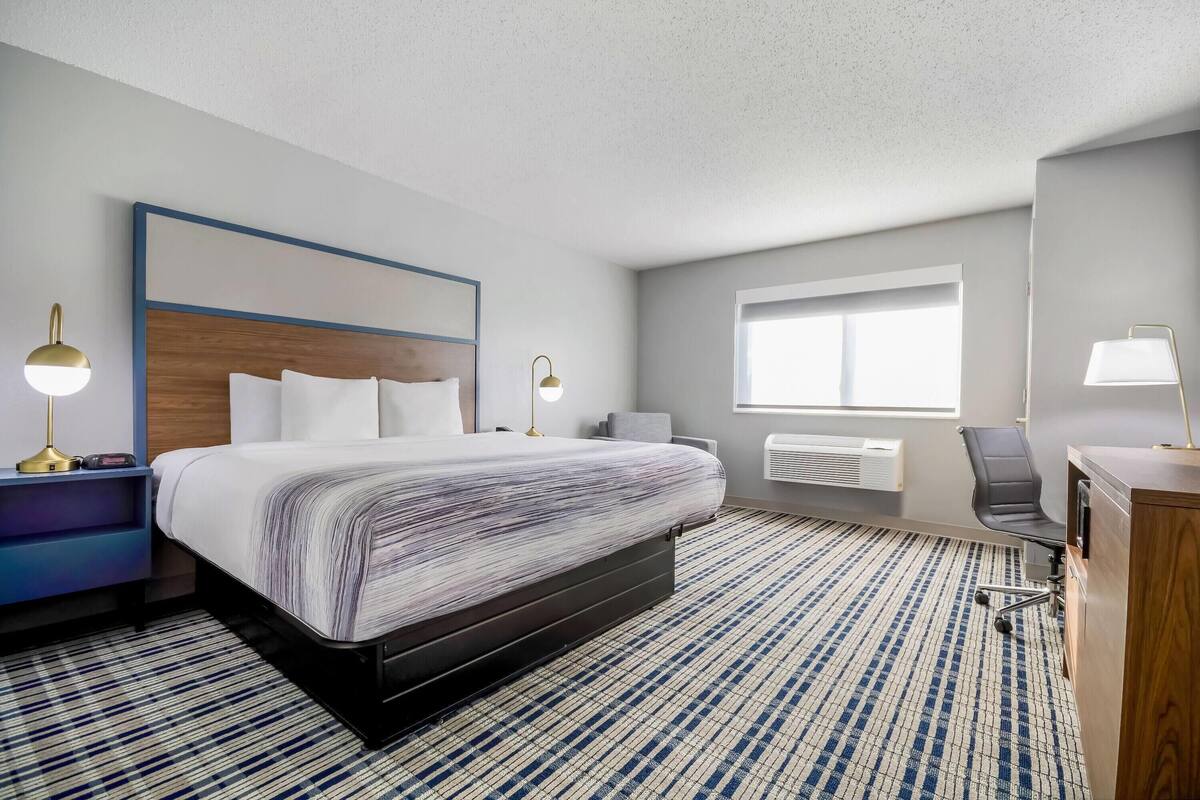 Een hotelkamer met een groot bed, nachtlampjes, een bureau met stoel, een raam en een radiator.