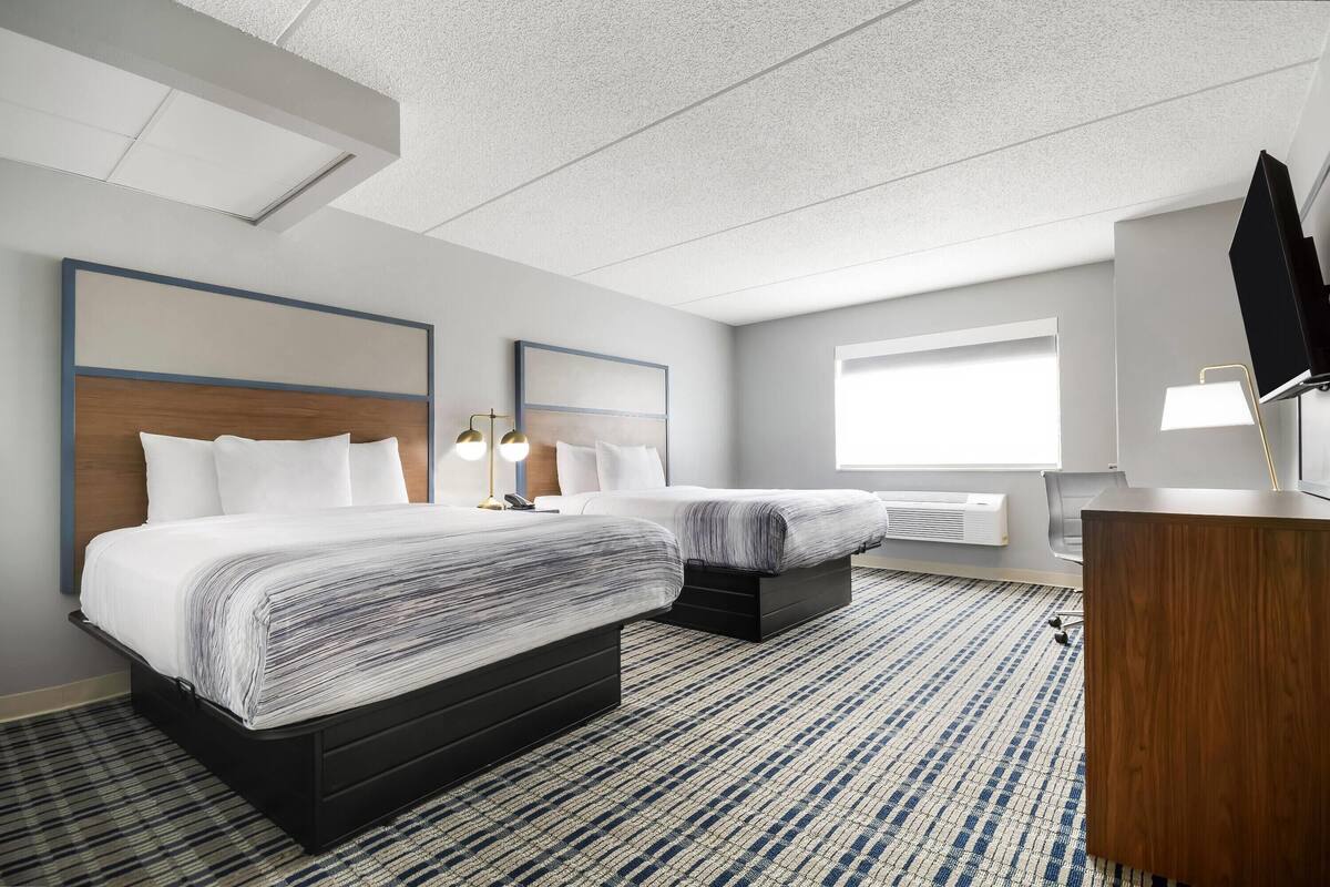 Een hotelkamer met twee bedden, een bureau, een televisie en een groot raam.