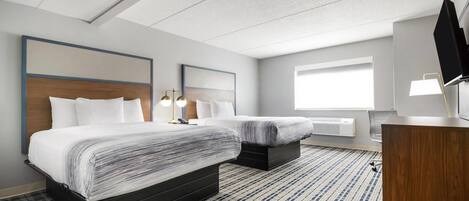 A hotel room with two beds, a desk, a TV, and a large window.