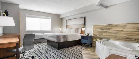 Quarto de hotel com cama, escrivaninha, cadeira e banheiro com banheira.