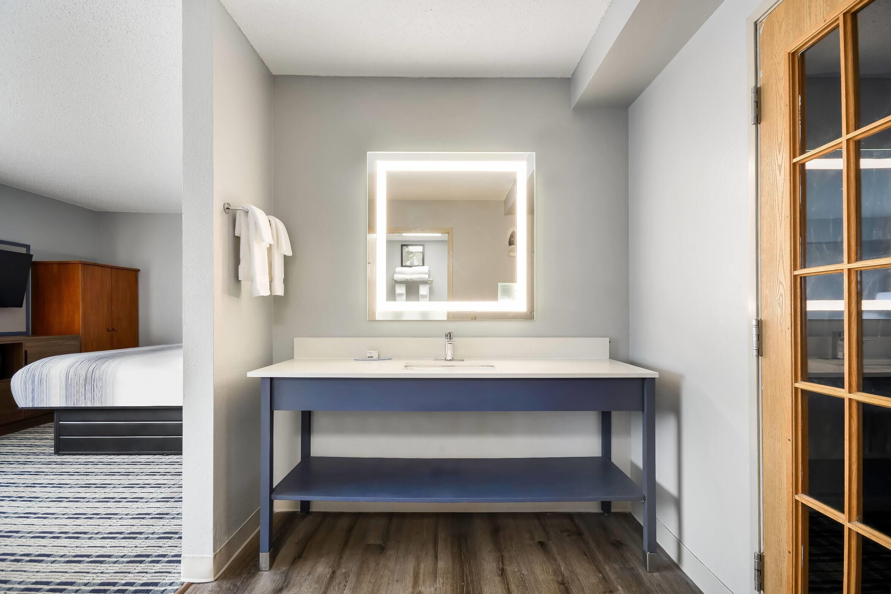 A modern bathroom with a large mirror, a white sink, and a wooden door.
