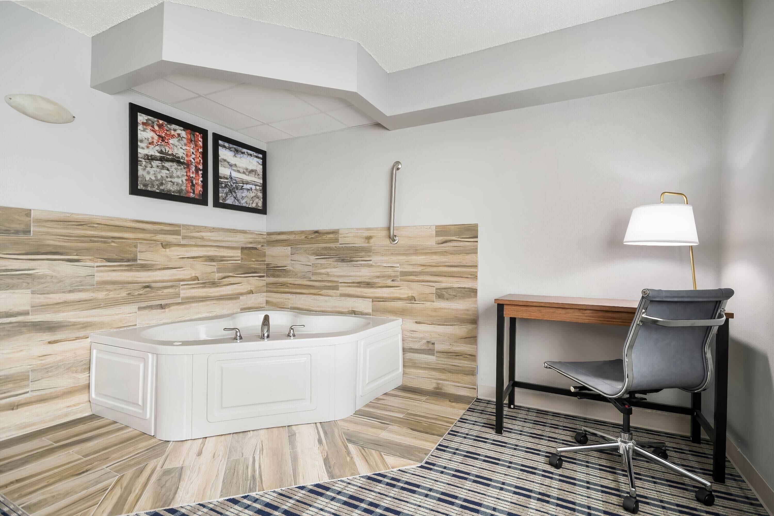 A modern bathroom with a freestanding bathtub, a wooden wall panel, a desk with a chair, and a handrail.