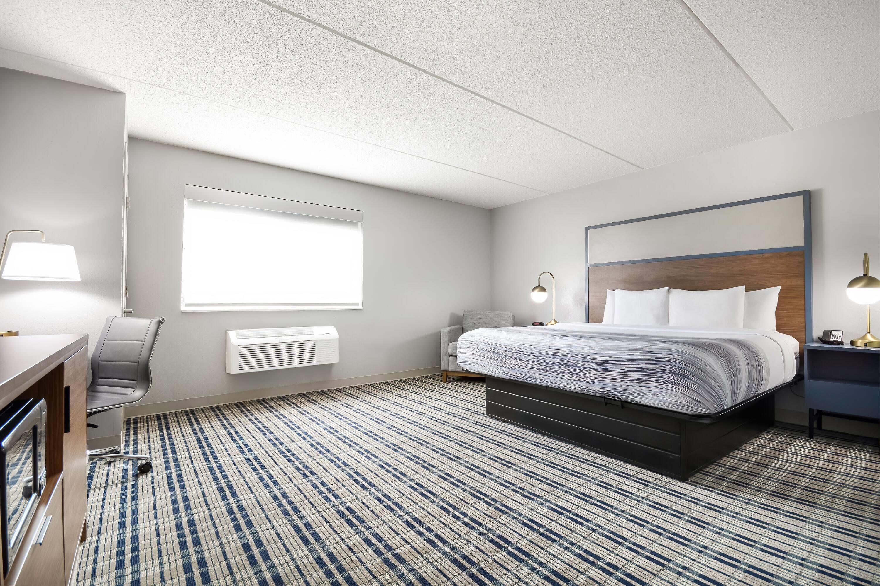 Habitación de hotel con cama, escritorio, silla y un ventanal grande.