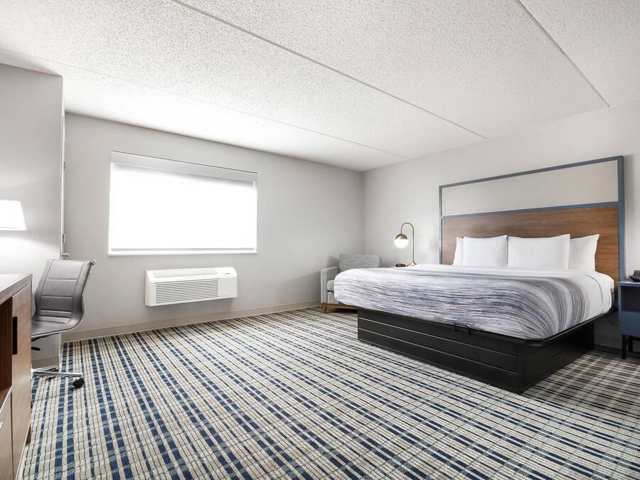 Habitación de hotel con cama, escritorio, silla y un ventanal grande.