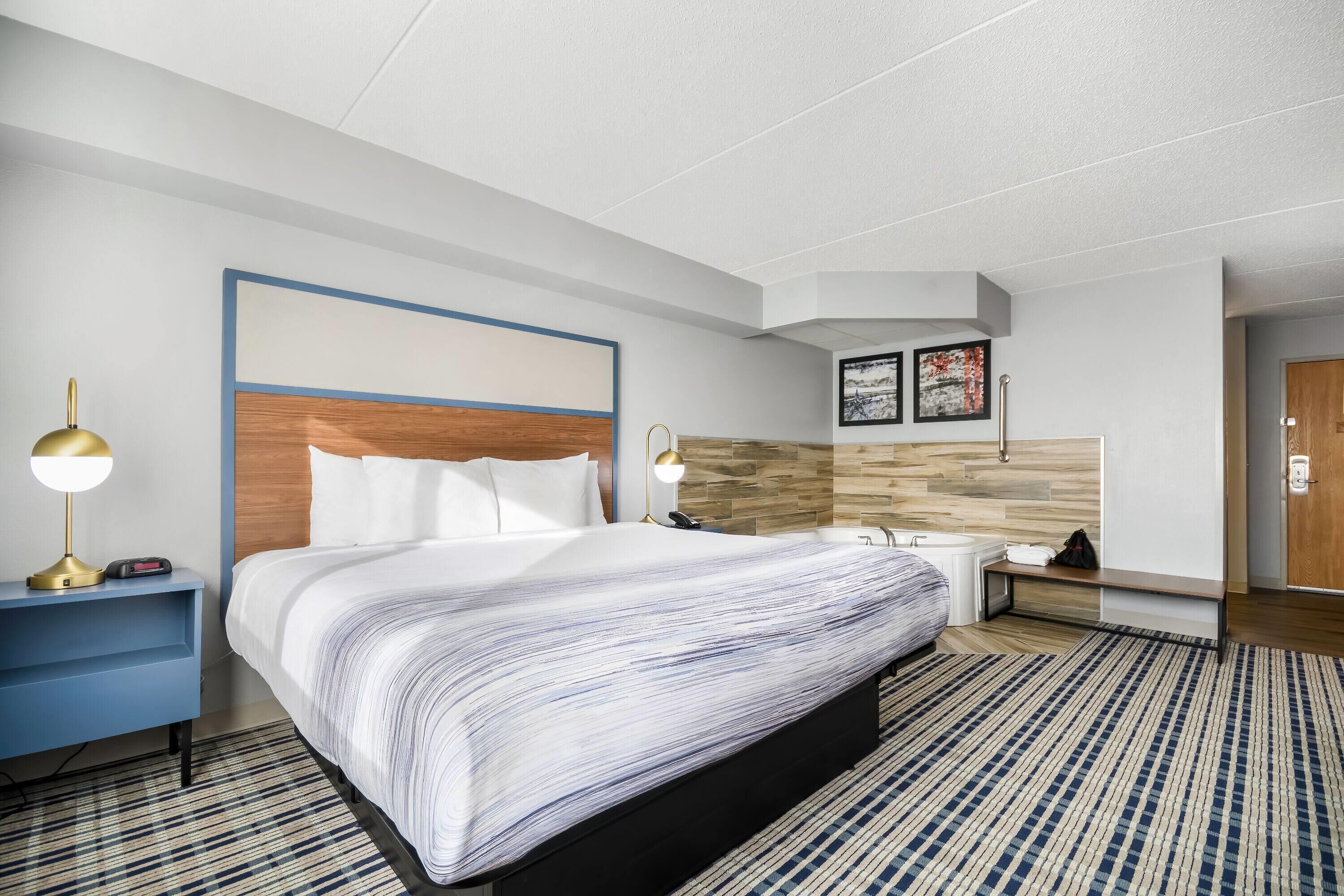 Een moderne hotelkamer met een groot bed, nachtkastjes, een bureau, een stoel, een wastafel en een spiegel.