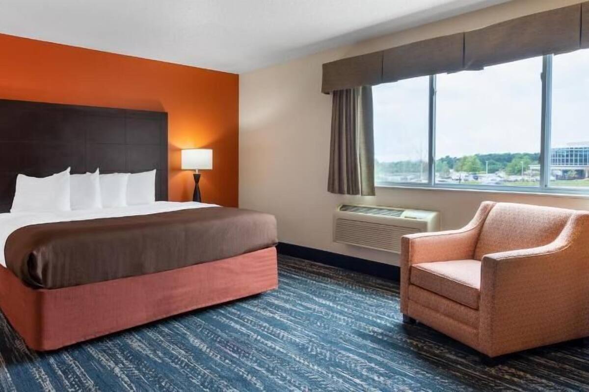 Een hotelkamer met een groot bed, twee nachtkastjes met lampen, een raam met uitzicht en een stoel.