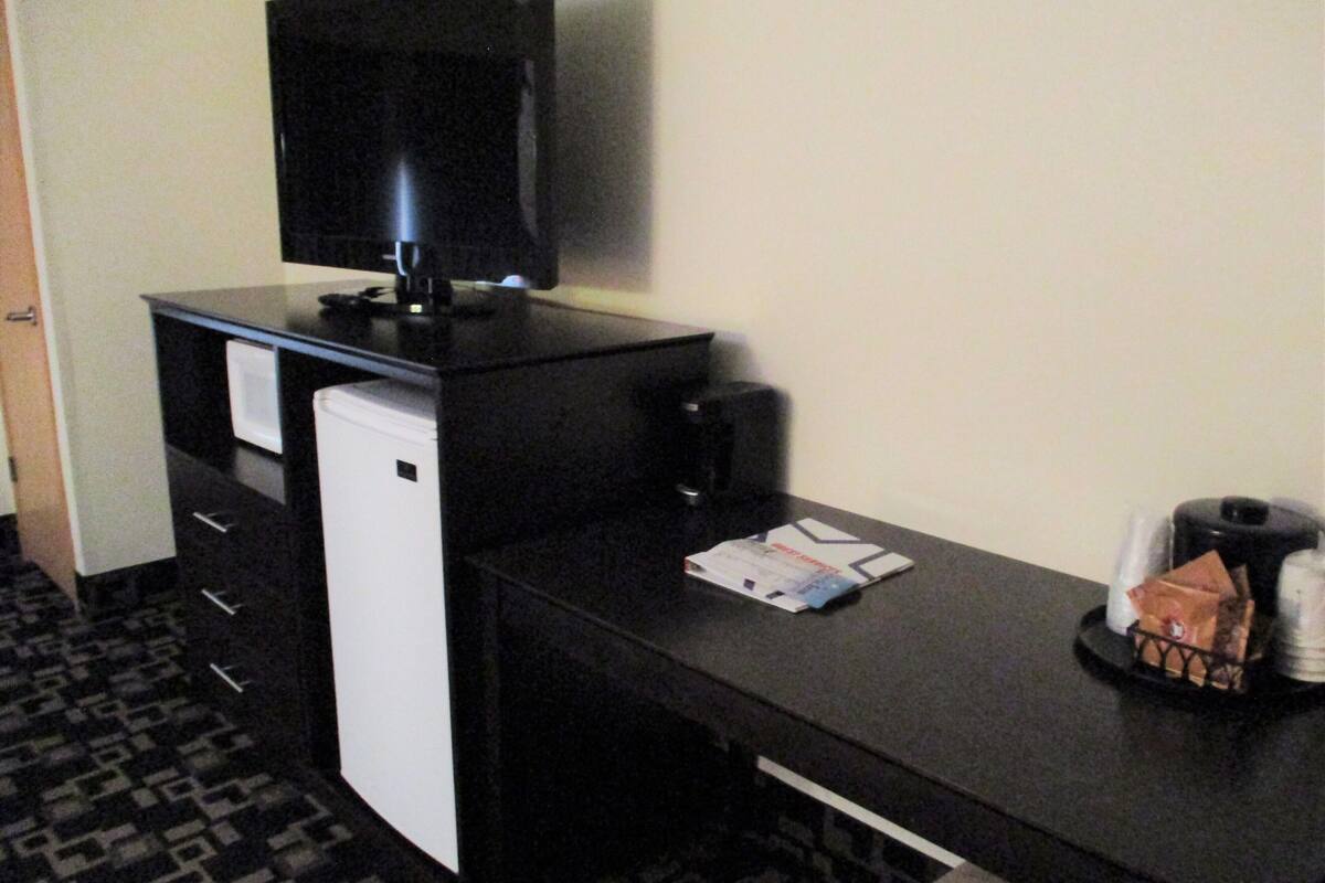 Een hotelkamer met een zwart bureau, een kleine witte koelkast, een televisie en een koffiezetapparaat.