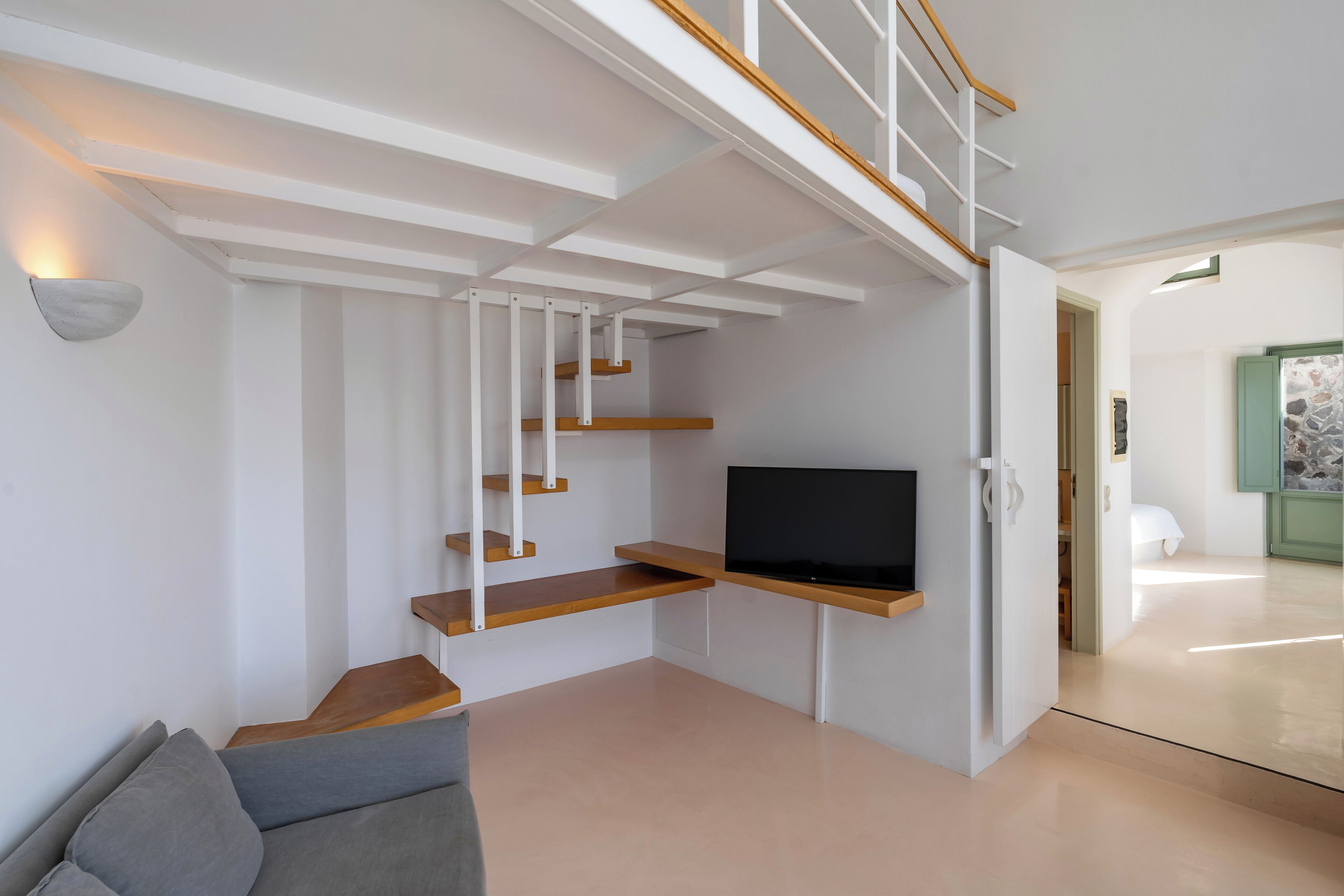 Una sala moderna con televisión empotrada, escalera de madera y un sofá gris.