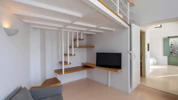 Una sala moderna con televisión empotrada, escalera de madera y un sofá gris.