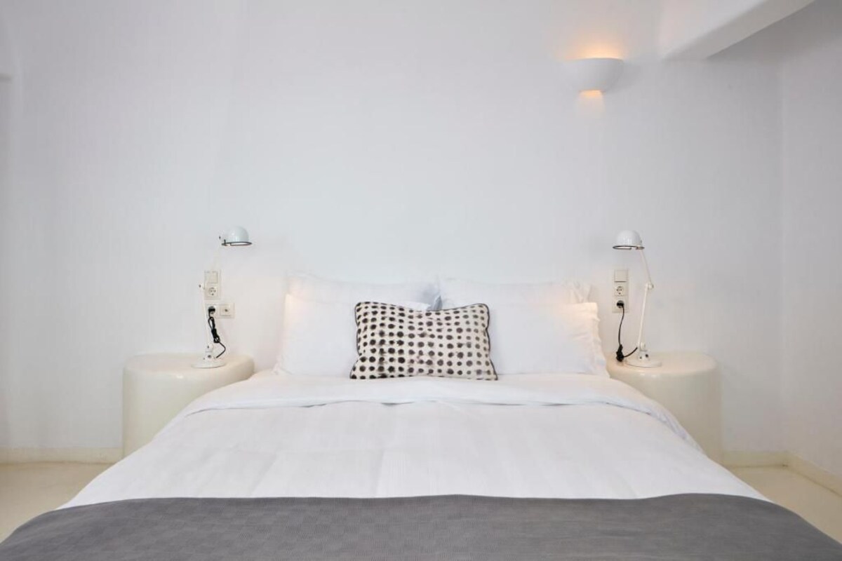 A minimalist bedroom with a large bed, two bedside tables, and a patterned pillow.