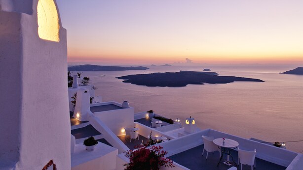 A white building with a balcony overlooking a calm sea and distant islands at sunset. - Cliff Side Suites (Santorini)