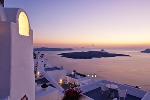 A white building with a balcony overlooking a calm sea and distant islands at sunset. - Cliff Side Suites (Santorini)