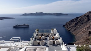 A rooftop terrace with white furniture and a clear view of the sea and distant islands. - Cliff Side Suites (Santorini)