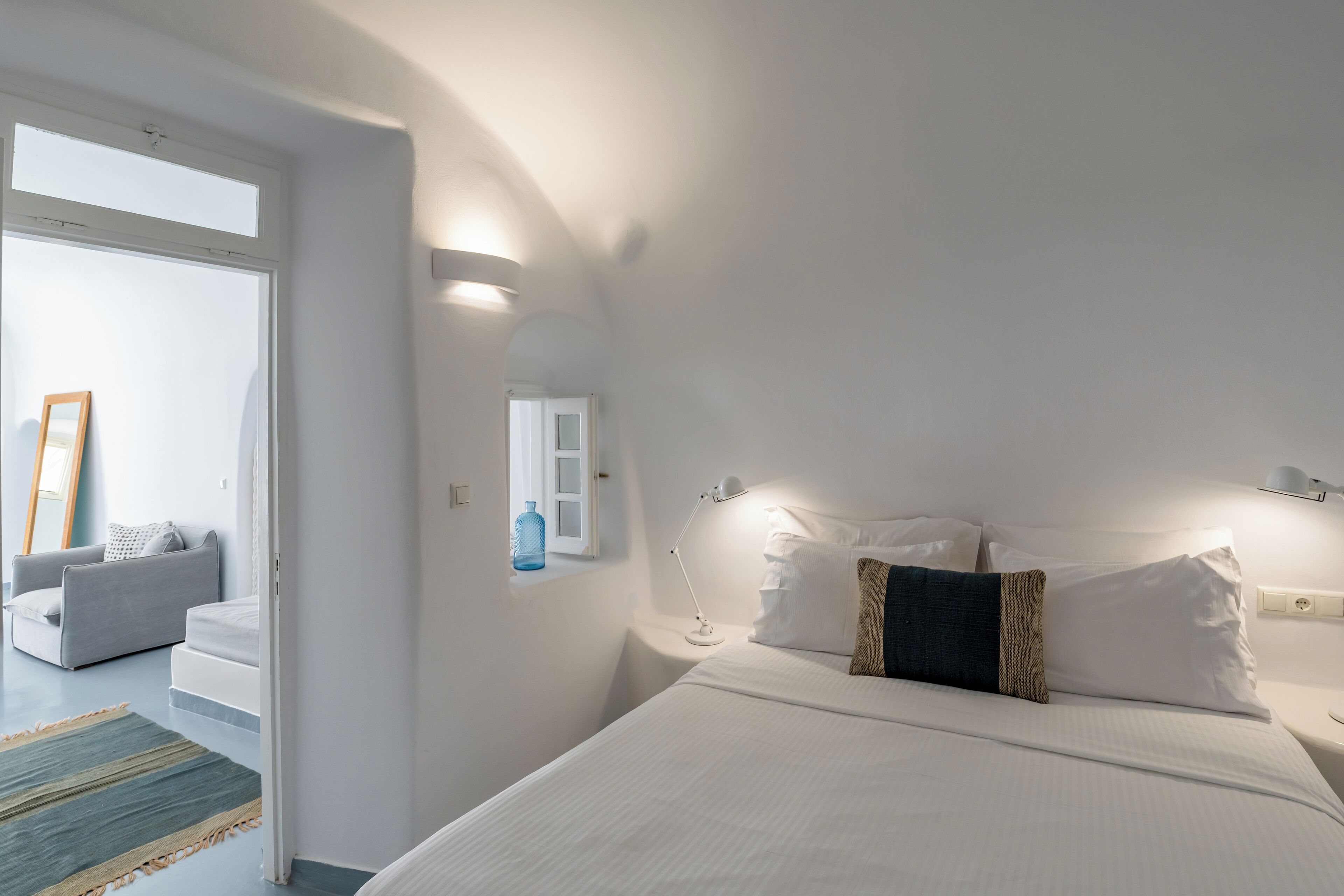 Ein modernes Hotelzimmer mit einem großen Bett, einem Nachttisch, einer Lampe, einem Fenster und Blick ins Freie.