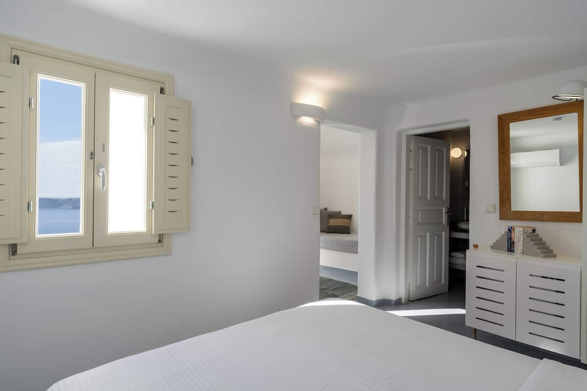 A bedroom with a bed, a wardrobe, a mirror, and a window with shutters.