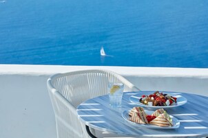Una mesa con un plato de comida y un vaso de agua en un balcón con vistas al mar.