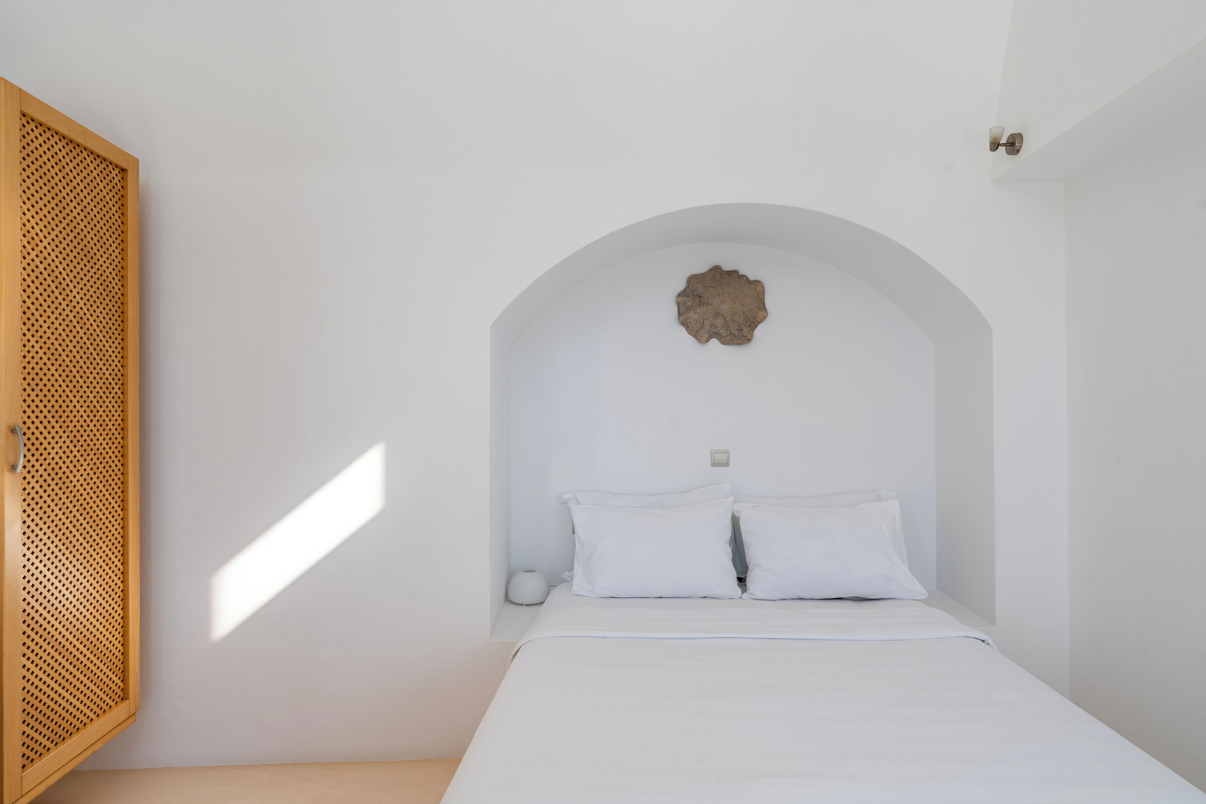 Ein Schlafzimmer mit einem Bett, weißen Wänden, einer Holztür mit Latten und einem außergewöhnlichen Deckenaufbau.