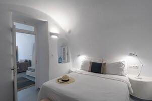 Un dormitorio con cama, lámparas de noche, un sombrero sobre la cama y una escalera que lleva a otra habitación.