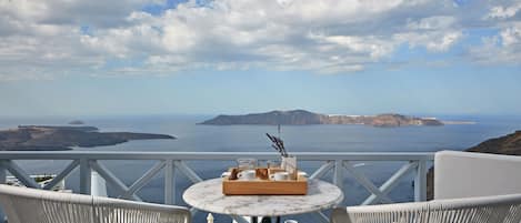 A terrace with wicker chairs and a table set with a tray of items, overlooking a coastal landscape with islands.