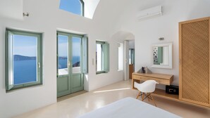 A modern hotel room with large windows, a bed, a desk, and a wardrobe. - Cliff Side Suites (Santorini)