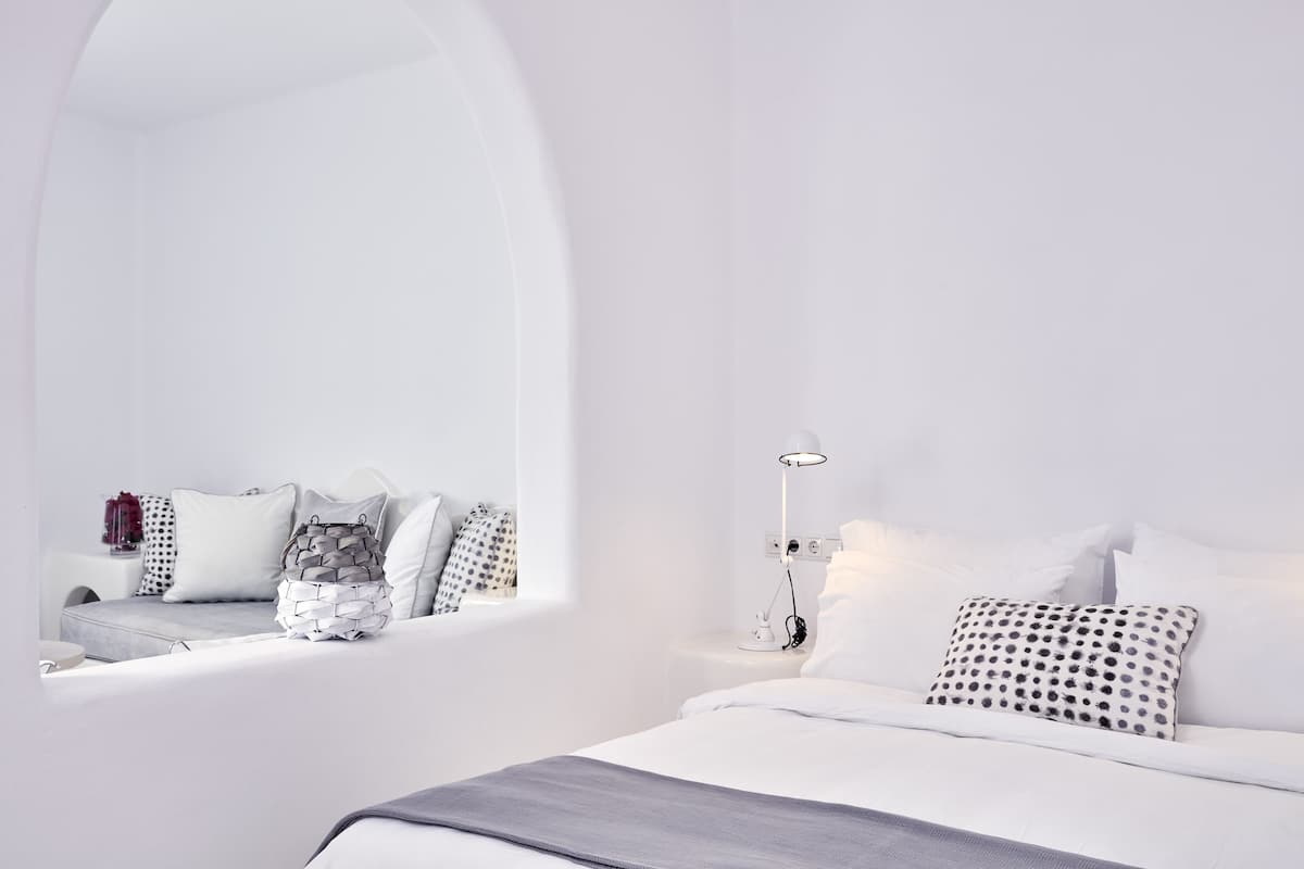 A minimalist bedroom with a large mirror, a bedside table with a lamp, and a neatly made bed.