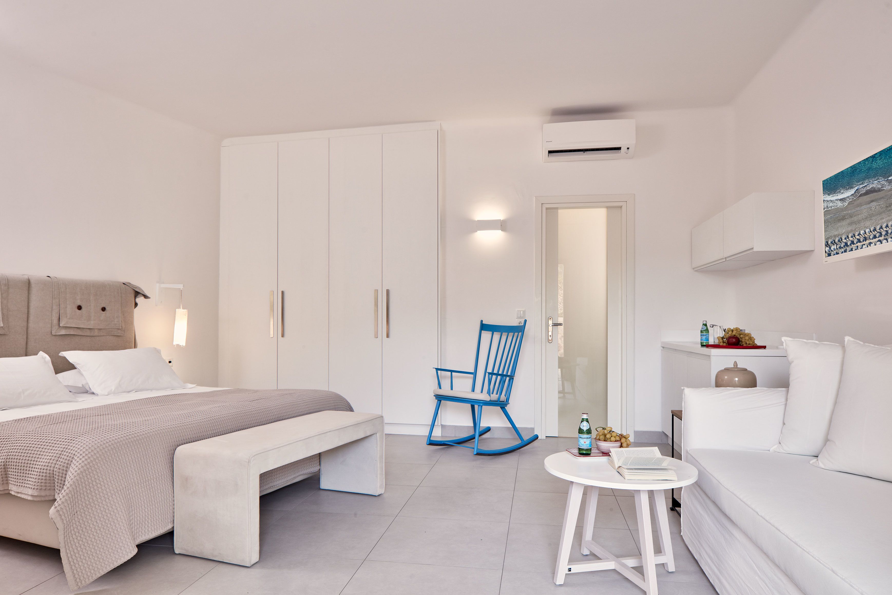 Un dormitorio moderno y minimalista con una cama, una mecedora, una mesita y un sofá.
