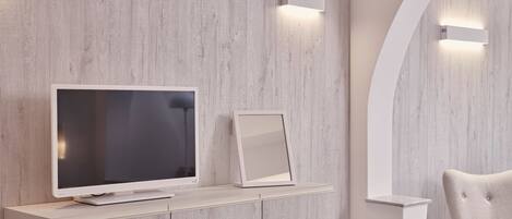Una sala de estar moderna con un televisor de pantalla plana sobre un mueble de madera clara, un cuadro enmarcado y un sillón capitonado.