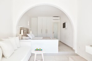 Un dormitorio moderno con decoración en tonos blancos, un sofá, una mesita con manzanas y un armario.