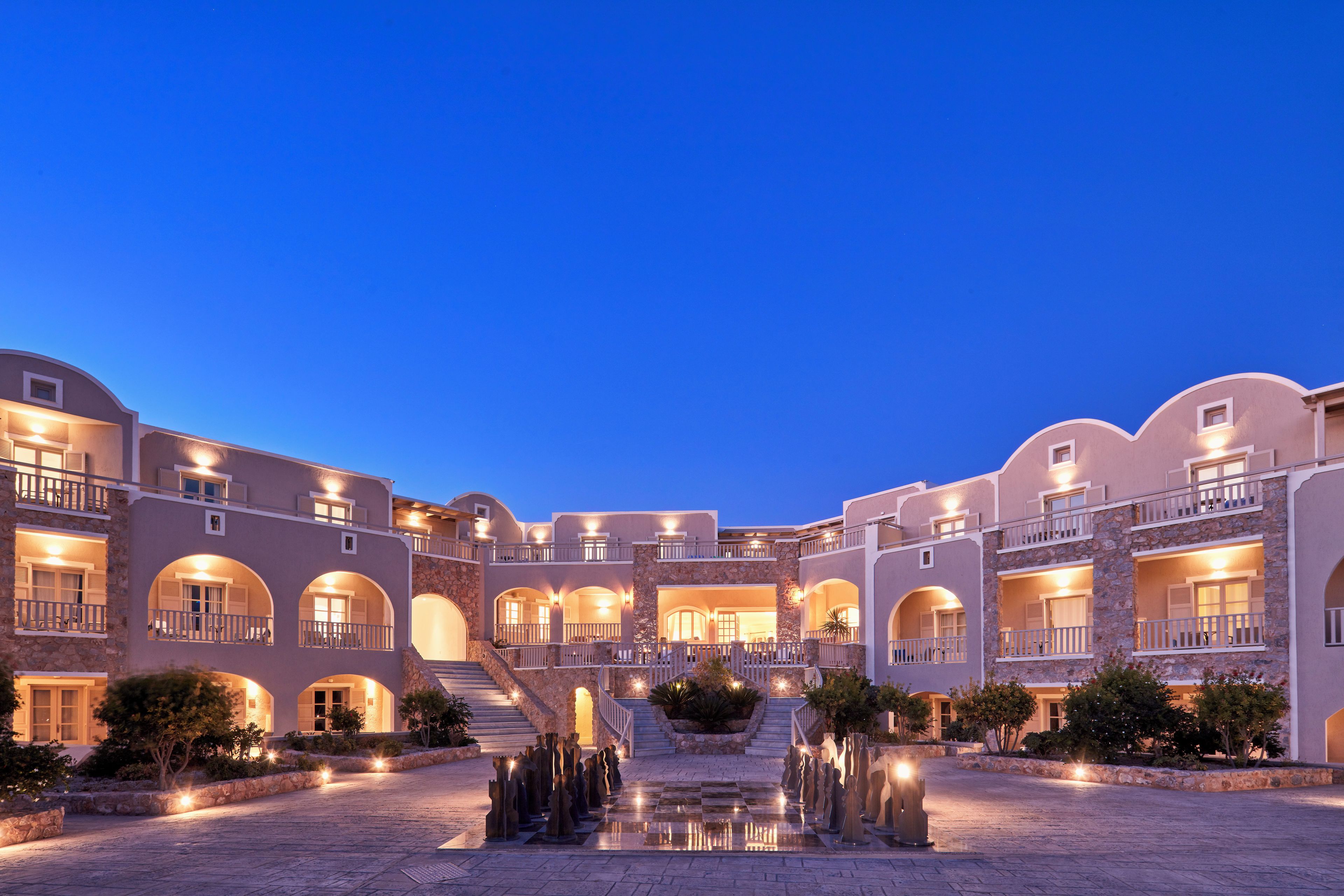 A multi-story hotel with a courtyard, featuring a central staircase, outdoor lighting, and a water feature.