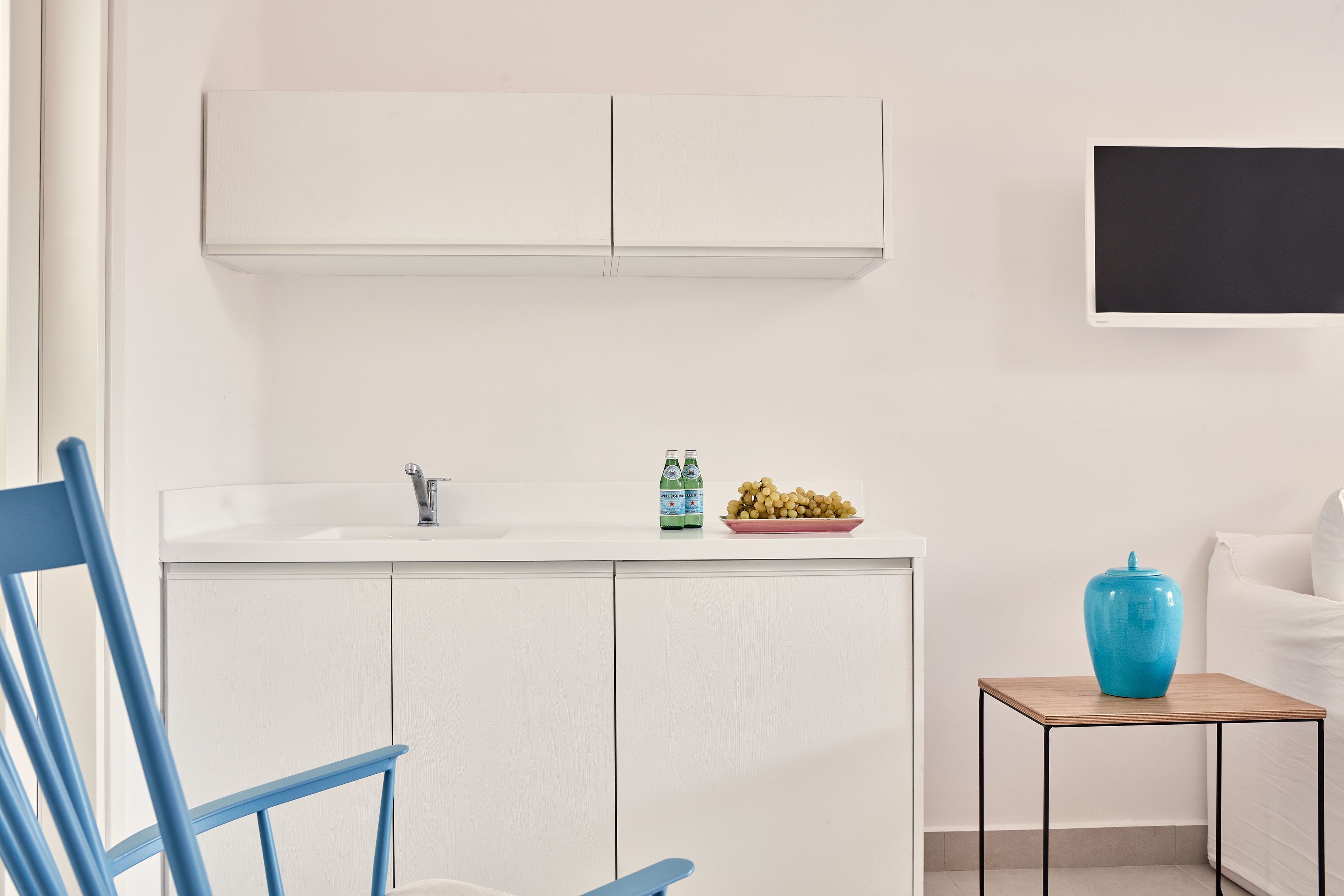 A modern kitchen with white cabinets, a sink, and a small table with a blue vase.